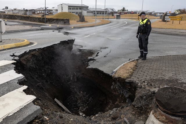 <p>A police officer stands by the crack in a road in the fishing town of Grindavik, Iceland</p>